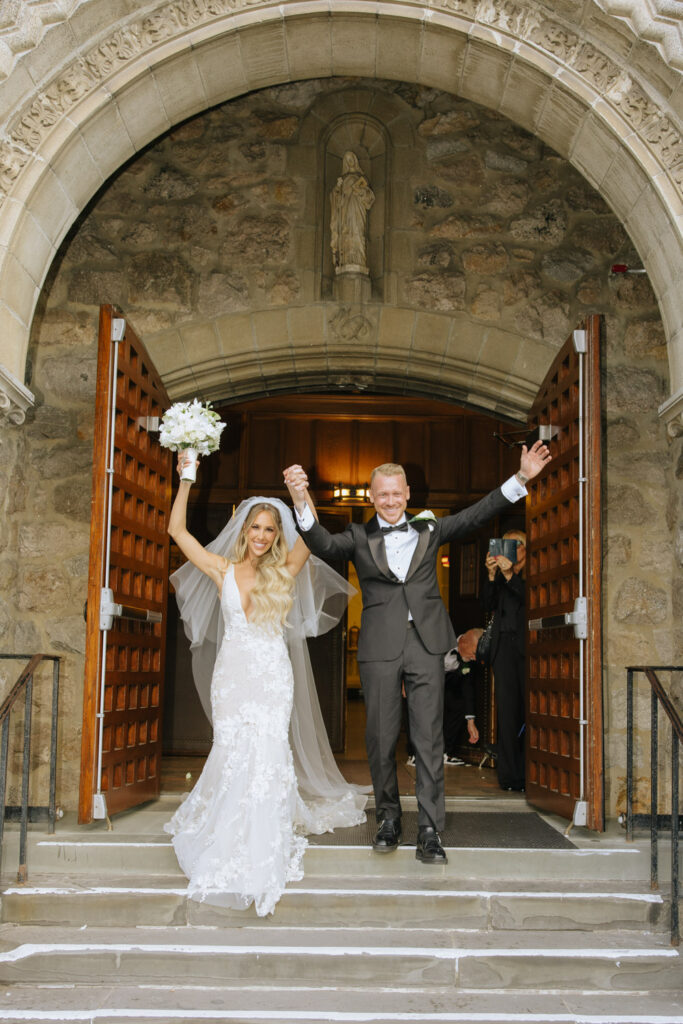 Russos On The Bay wedding photographer captures A newlywed couple exits a Catholic ceremony at Russos on the Bay, celebrating with raised arms.