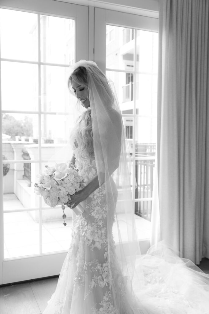 A bride in a white gown and veil holds a white floral bouquet at Russos on the Bay wedding.