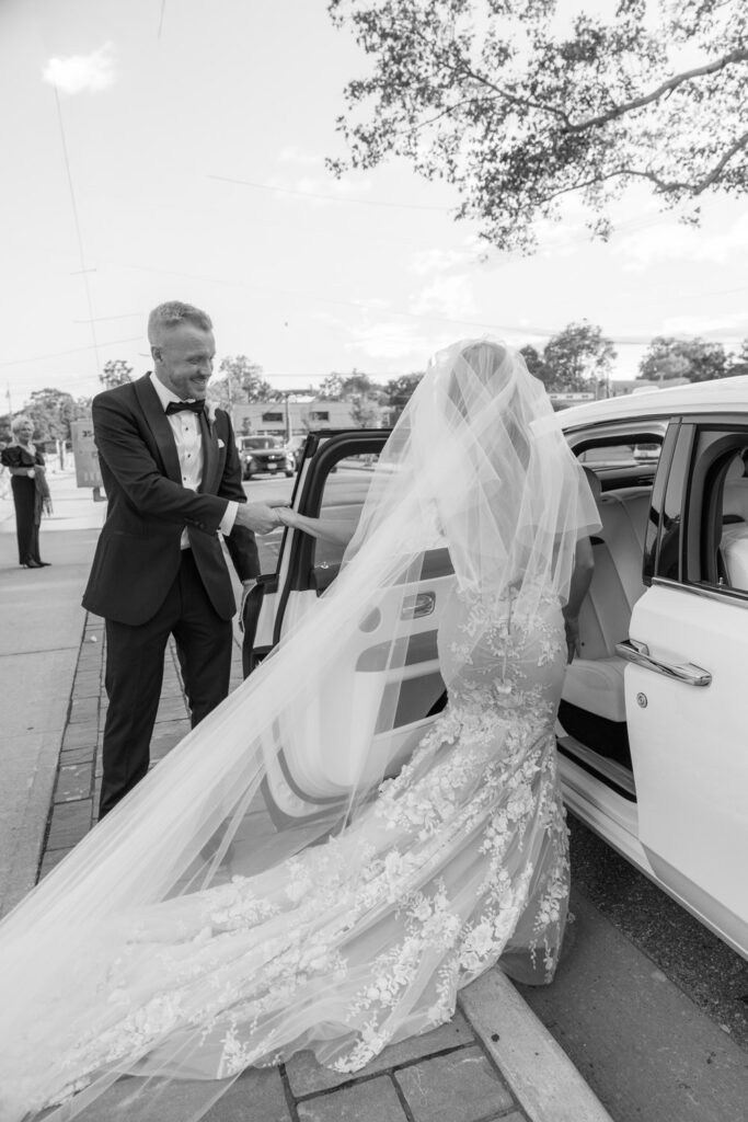 Groom helps his bride step into a white Rolls-Royce during a wedding at Russos on the Bay.