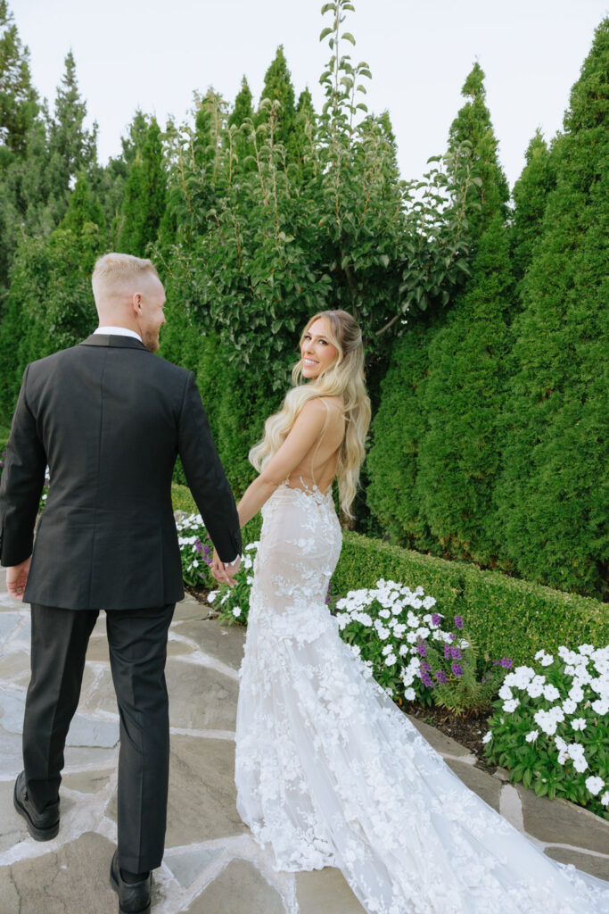 A newlywed couple walks hand in hand on a path at their Russos on the Bay wedding.