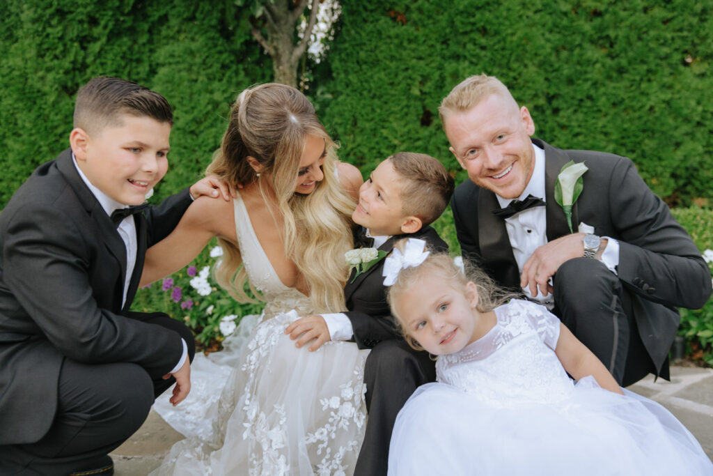 The wedding couple smiles with three children outdoors at a Russos on the Bay wedding.