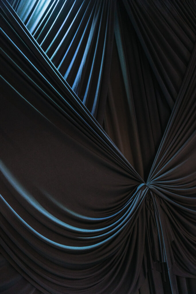 Dark, draped fabric gathered in the center and lit by blue light at a Russo's On The Bay wedding.