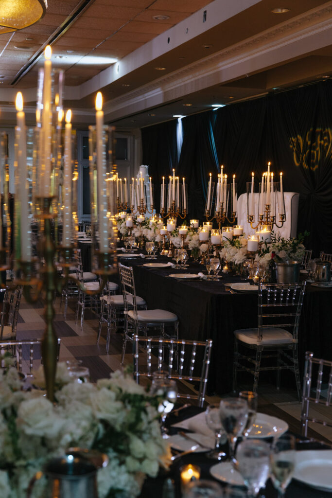 A long table with a black tablecloth is set with white flowers and candelabras at a Russos on the Bay wedding.