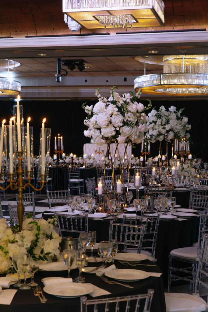 Reception tables set with black linens, clear chairs, and white floral centerpieces at Russos on the Bay.