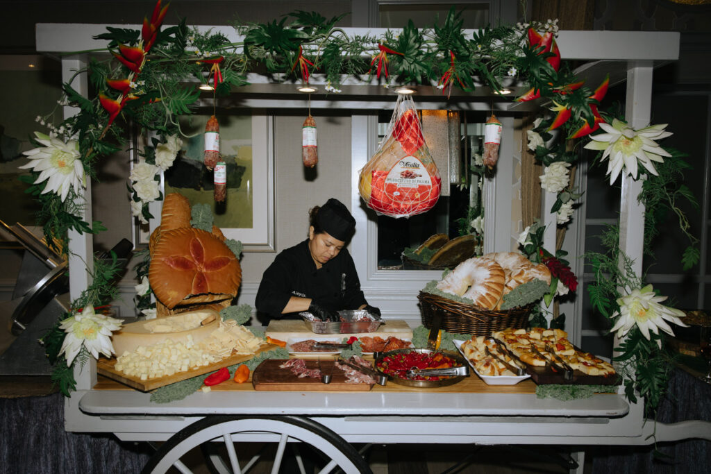 A chef prepares a charcuterie spread on a decorated cart at a Russos on the Bay wedding.
