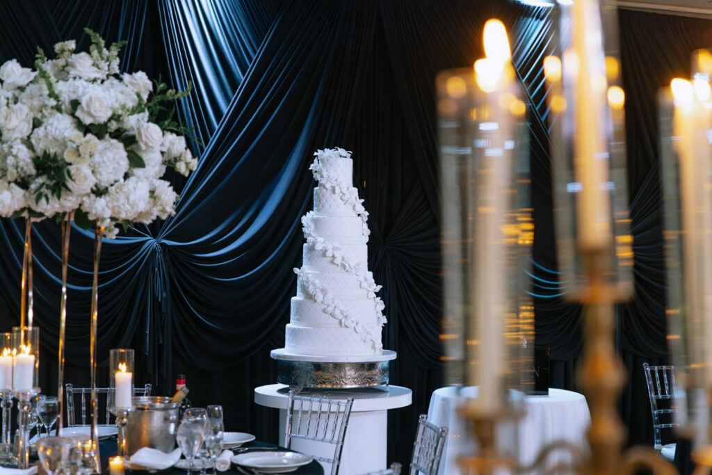 A white multi-tiered wedding cake with white floral accents at a Russos on the Bay wedding reception.