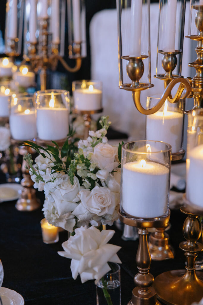White roses and candles in glass holders decorate a black table at a Russos on the Bay wedding.