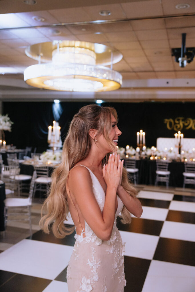 A smiling bride stands on a black and white checkered floor at a wedding reception at Russos on the Bay.