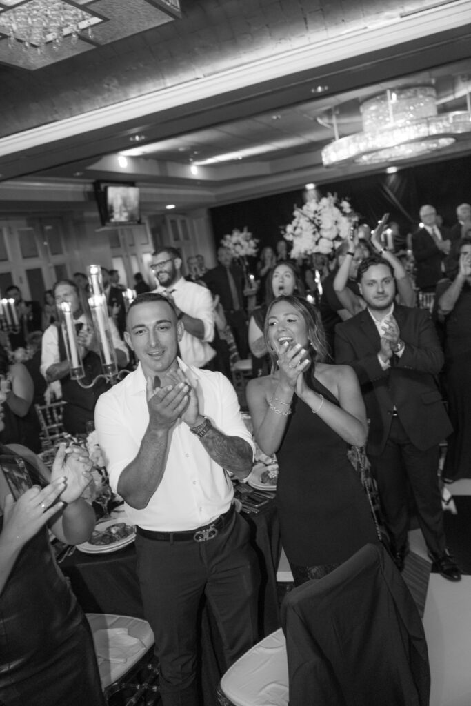 Guests clap, some with open mouths, during a wedding reception at Russo's On The Bay.