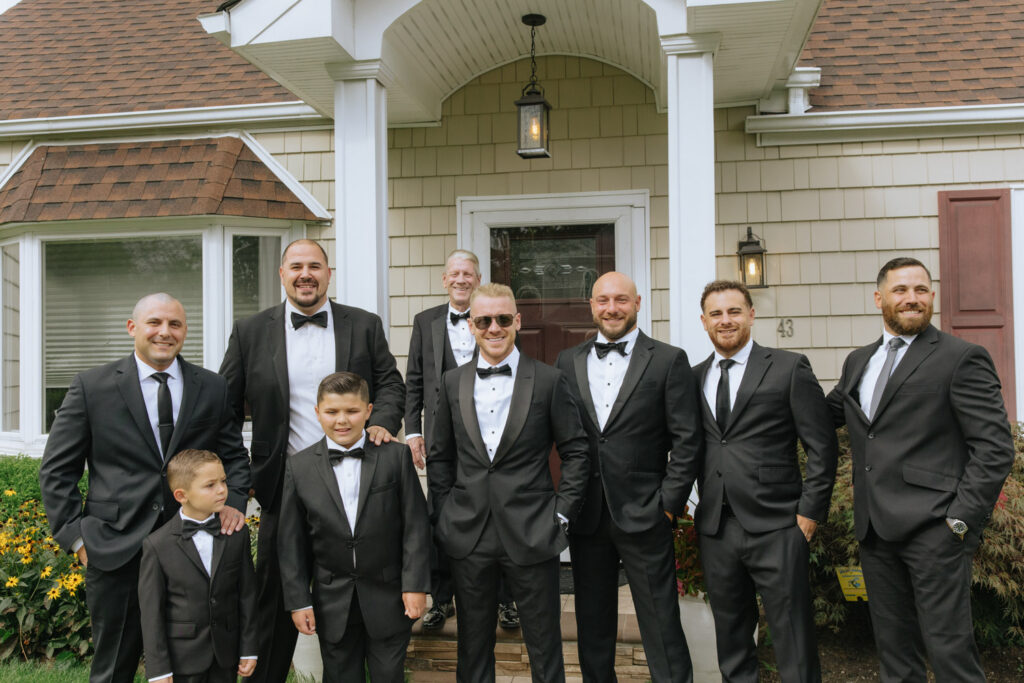 A group of men in black tuxedos pose for a photo at a Russos on the Bay wedding.