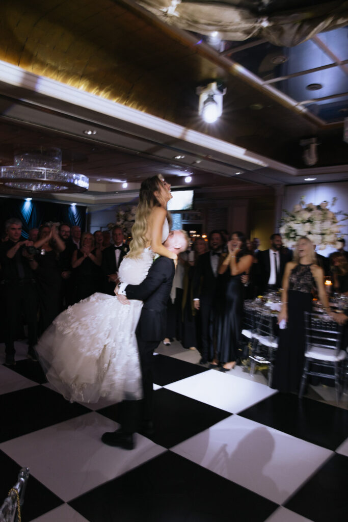 Groom lifts bride on a black and white checkered dance floor at a Russos on the Bay wedding.