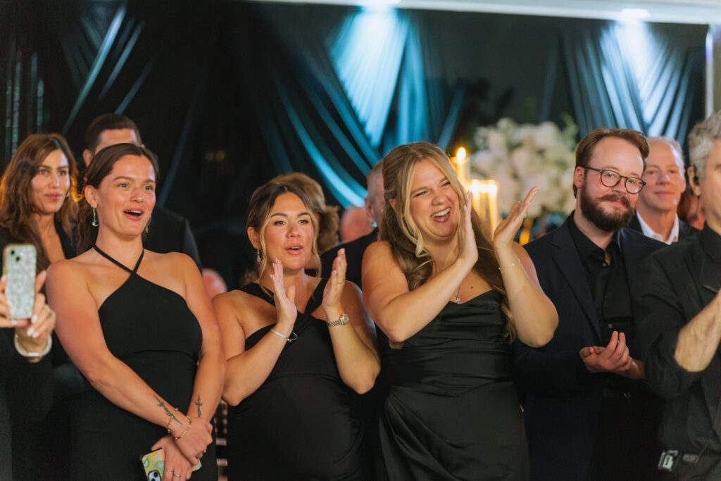 Guests in black attire watching a performance with some clapping at a Russos on the Bay wedding.