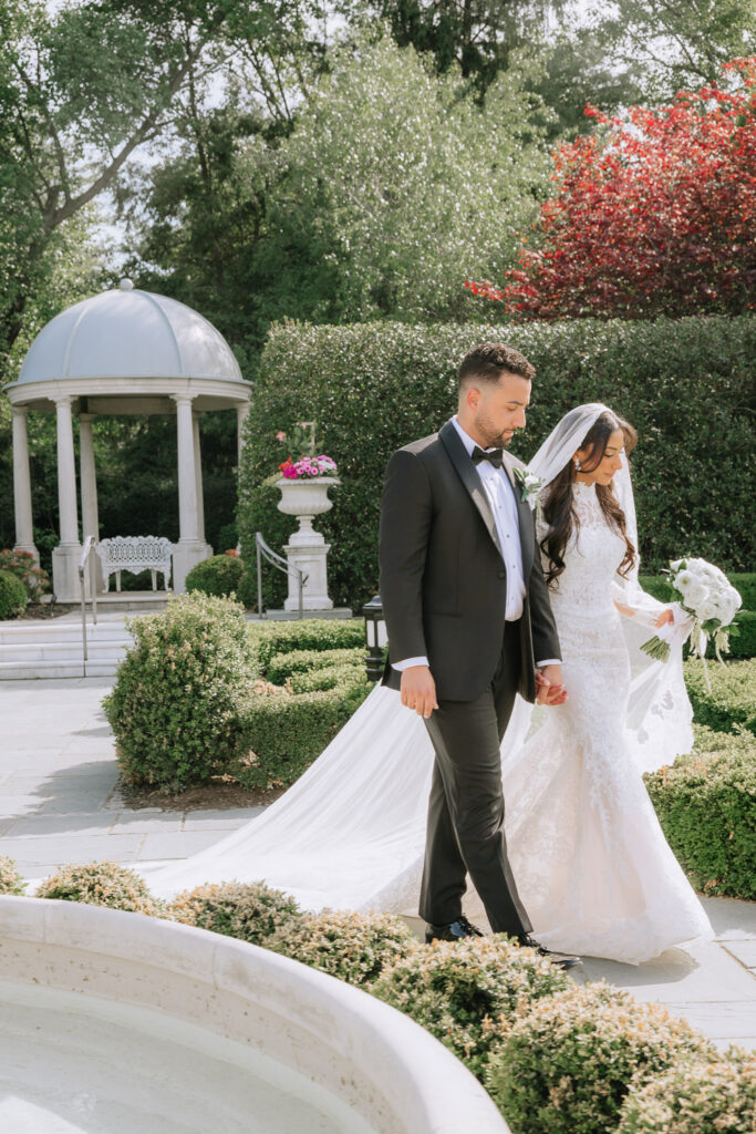 A newlywed couple walks hand-in-hand through the formal gardens at Park Château Estate & Gardens.