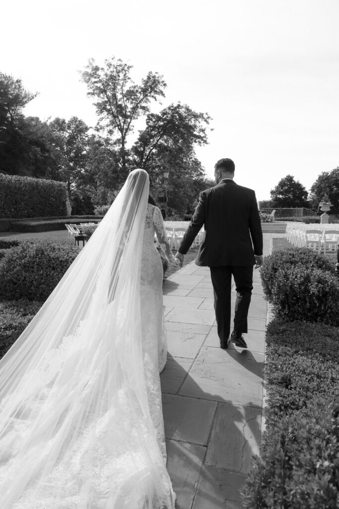 A bride and groom walk hand-in-hand down a paved path at Park Chateau in New Brunswick, New Jersey.