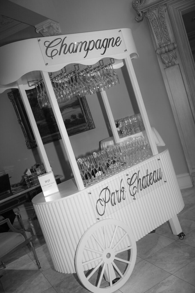 A white champagne cart with "Champagne" and "Park Chateau" signs, holding many empty flutes.