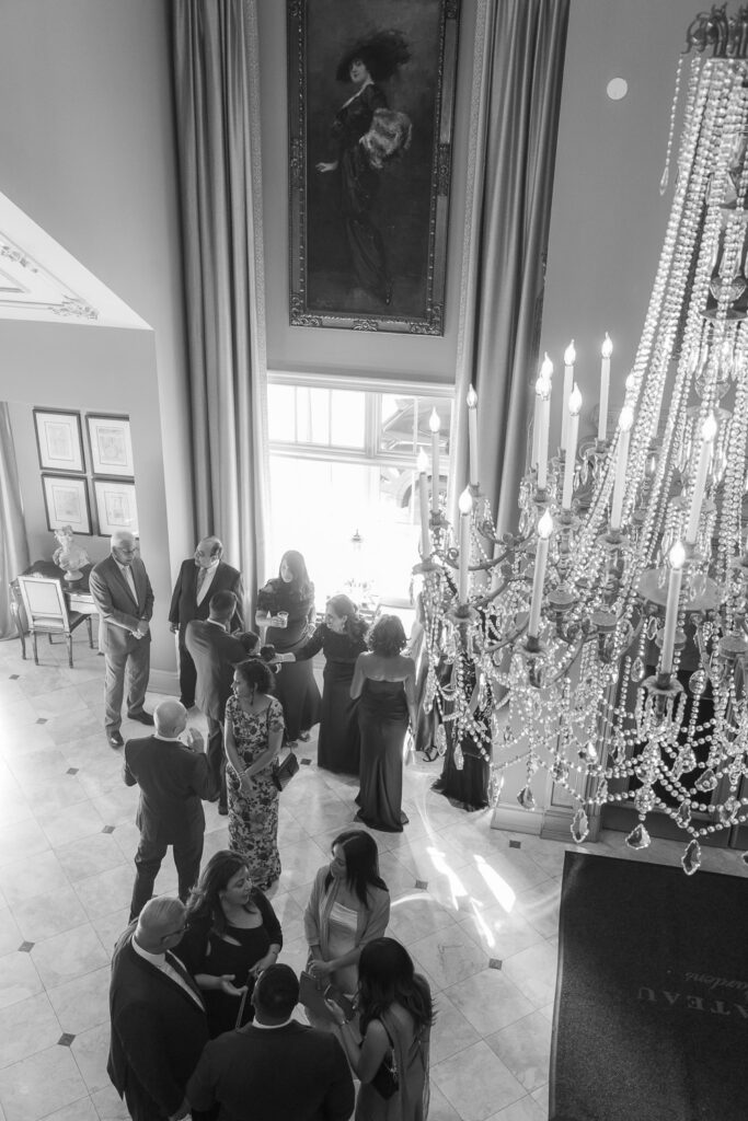 Wedding guests gather in a grand hallway with a large chandelier at Park Chateau New Brunswick, New Jersey.