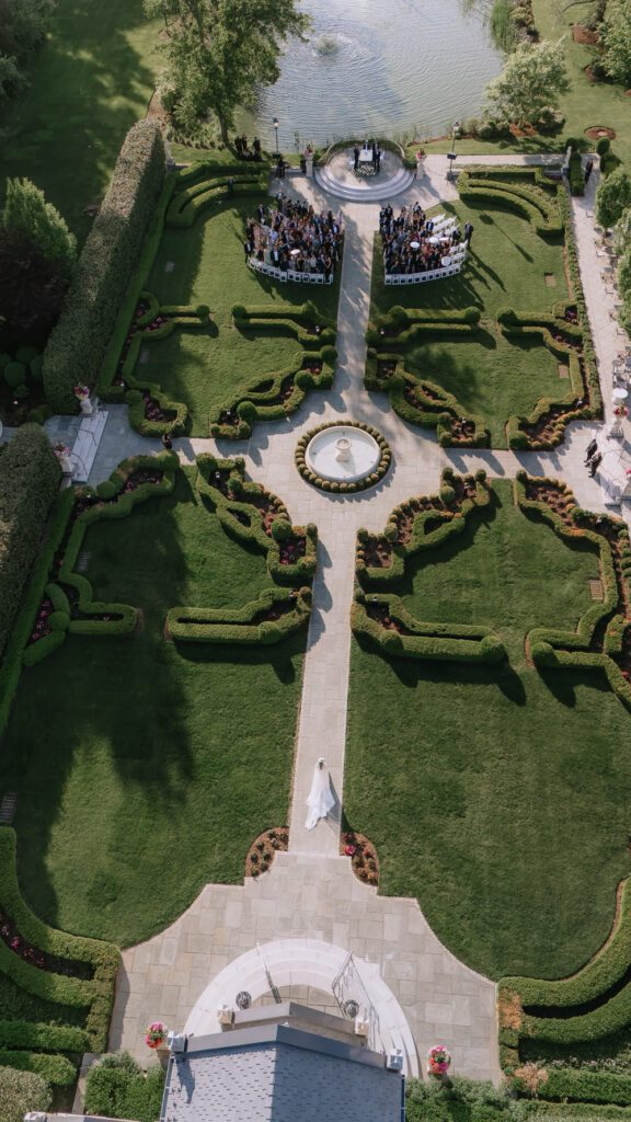 A bride walks down a paved path surrounded by gardens toward wedding guests at Park Château Estate.