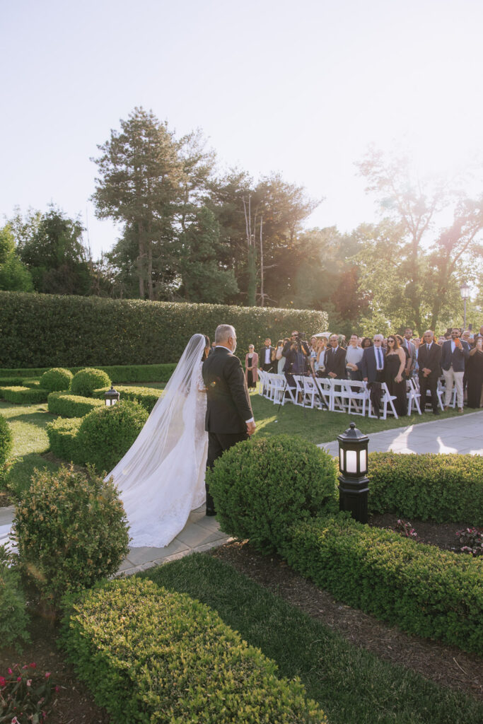 Bride and father walk down the aisle at an outdoor Park Chateau wedding ceremony in New Brunswick, NJ.