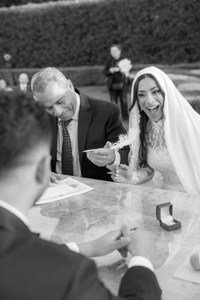 Man signs official documents with a feather pen at a Park Chateau Palestinian-Egyptian Muslim wedding.