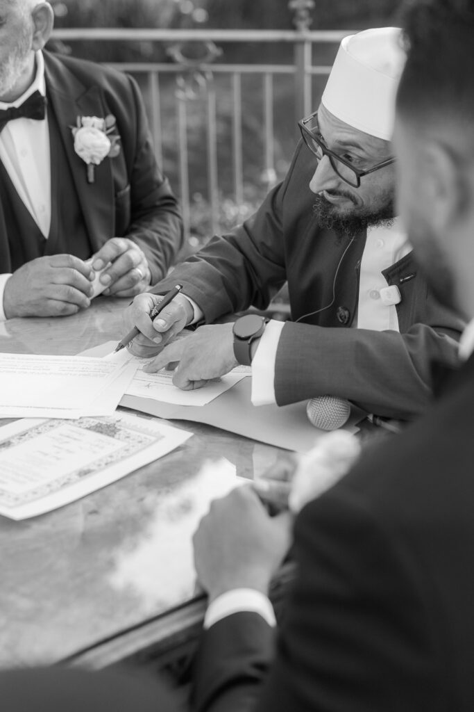 A man in a kufi and glasses signs paperwork during a Palestinian-Egyptian Muslim wedding at Park Chateau.