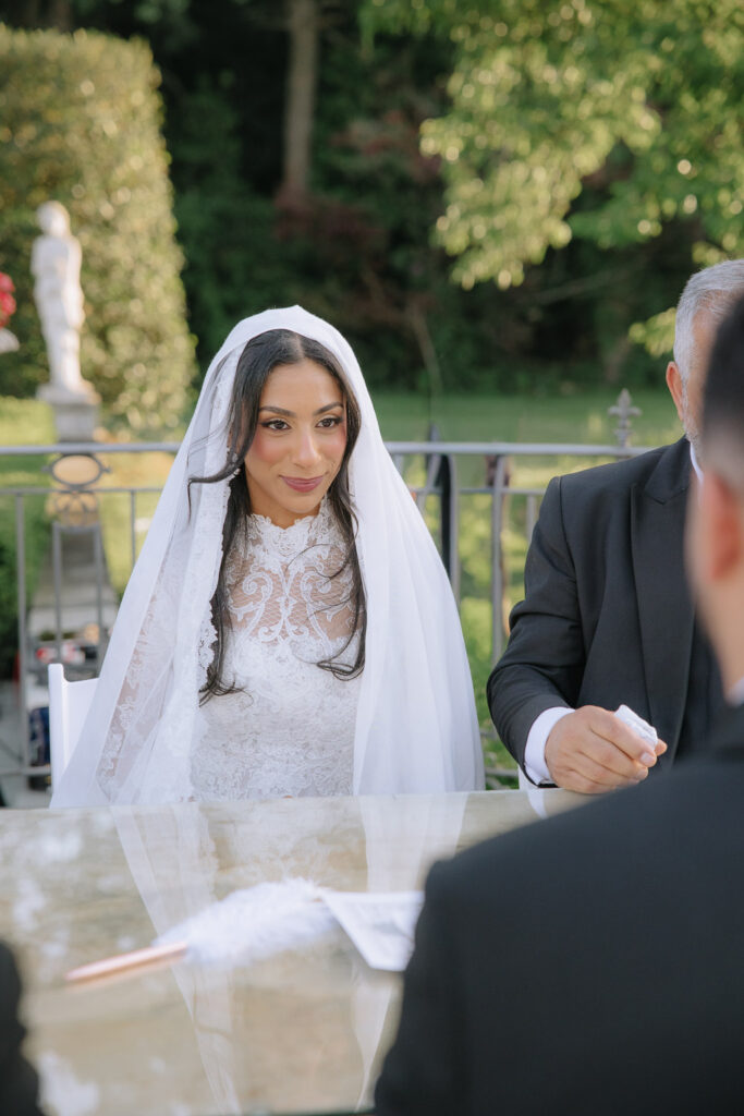 A bride in a white lace dress and veil sits at a table during a Park Chateau Estate wedding.