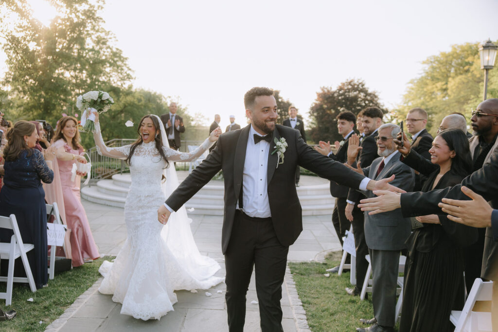 Menah and Ashraf walk through guests cheering at their Park Château Estate & Gardens wedding.