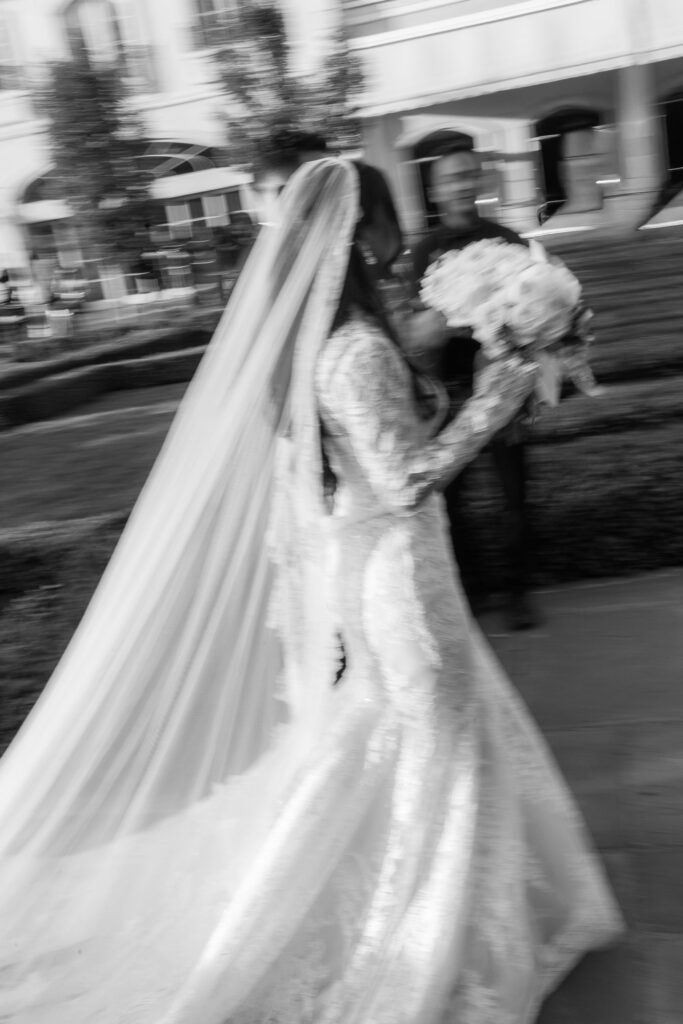 A bride in a long gown and veil walks, holding a bouquet at a Park Château wedding.