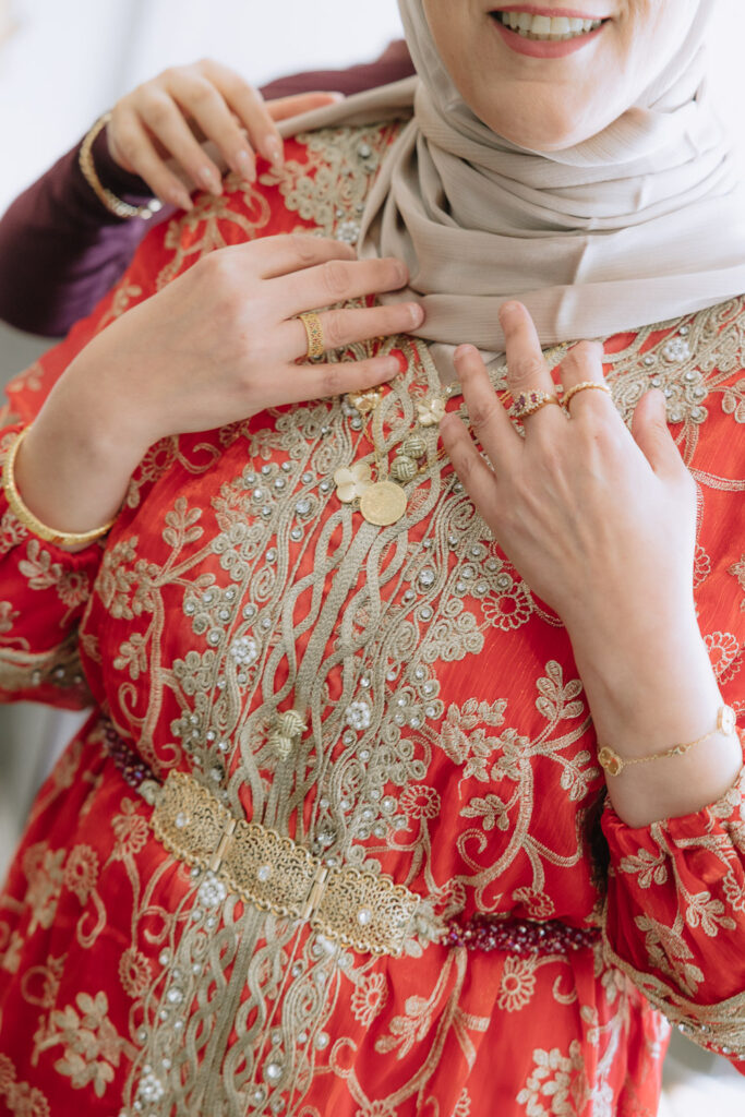 Woman in an ornate red and gold dress adjusts her neutral-colored headscarf at Park Chateau.