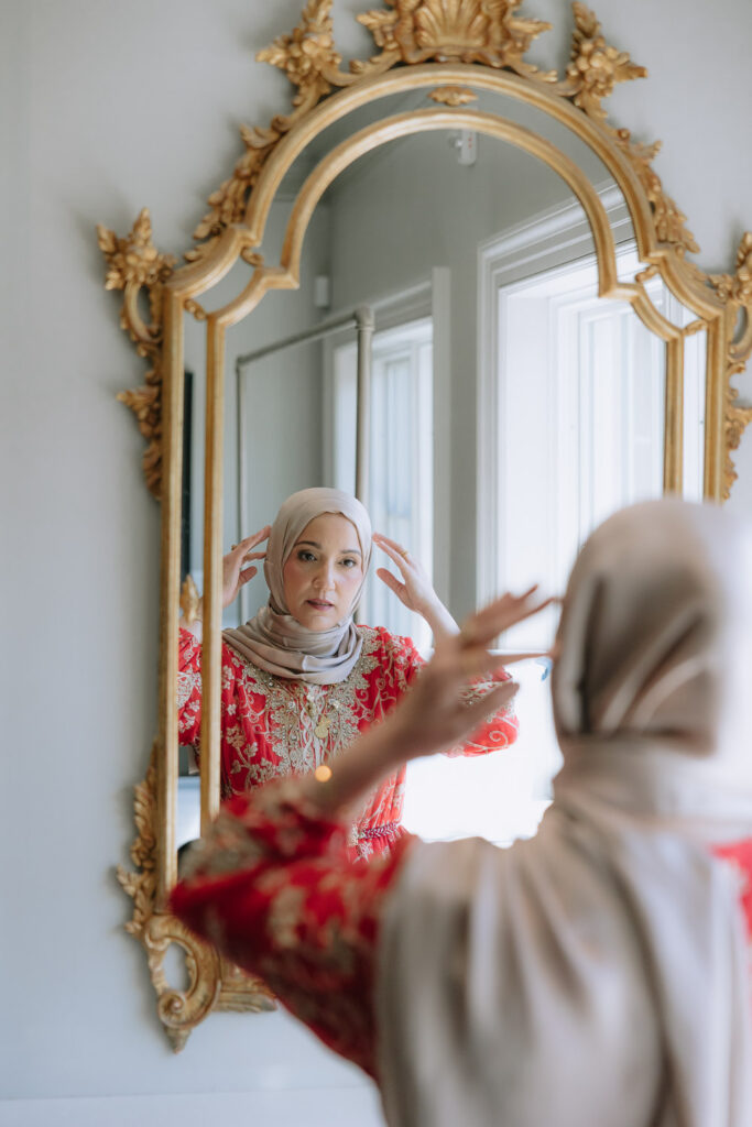 Woman adjusts her hijab in a decorative mirror at a Park Chateau wedding in New Brunswick, NJ.