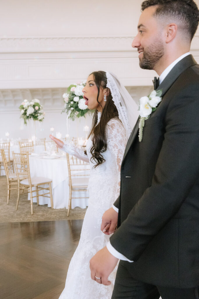 A bride with an open mouth and groom walk past wedding reception tables at Park Chateau.