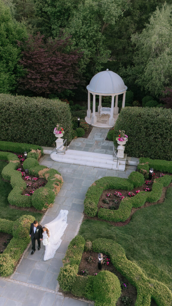 A newlywed couple walks hand in hand through the formal gardens of Park Château Estate & Gardens.