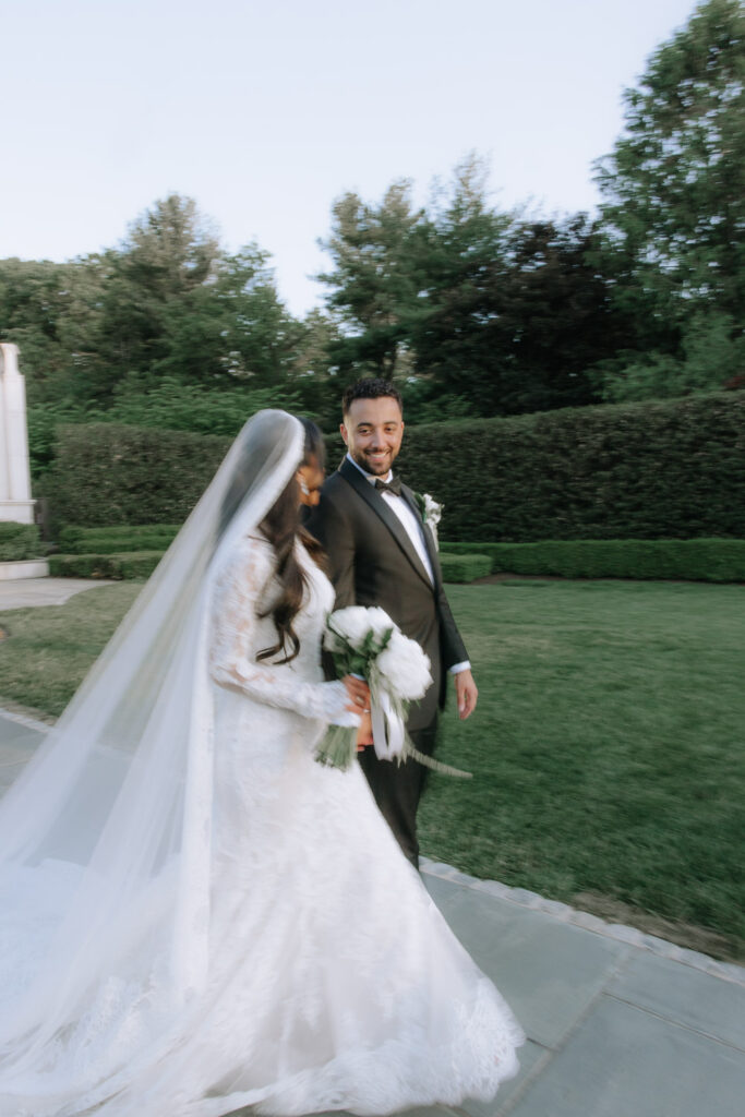 A groom smiles as he walks next to his bride holding a white bouquet at Park Chateau in New Jersey.