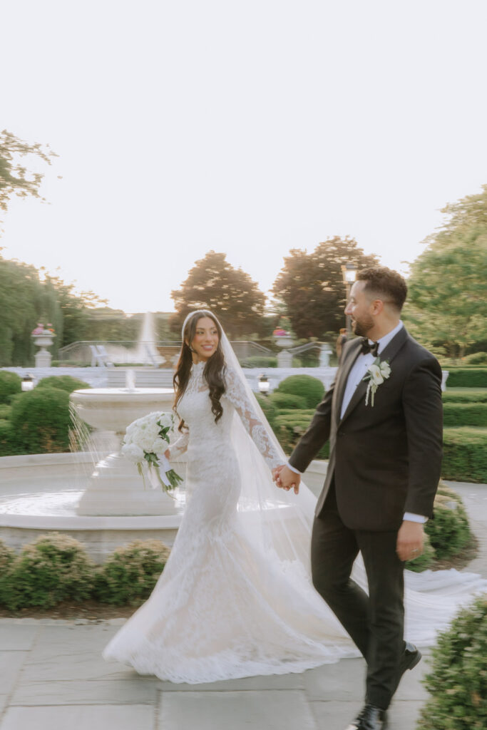 A newlywed couple walks hand-in-hand past a fountain during their Park Chateau wedding in New Jersey.