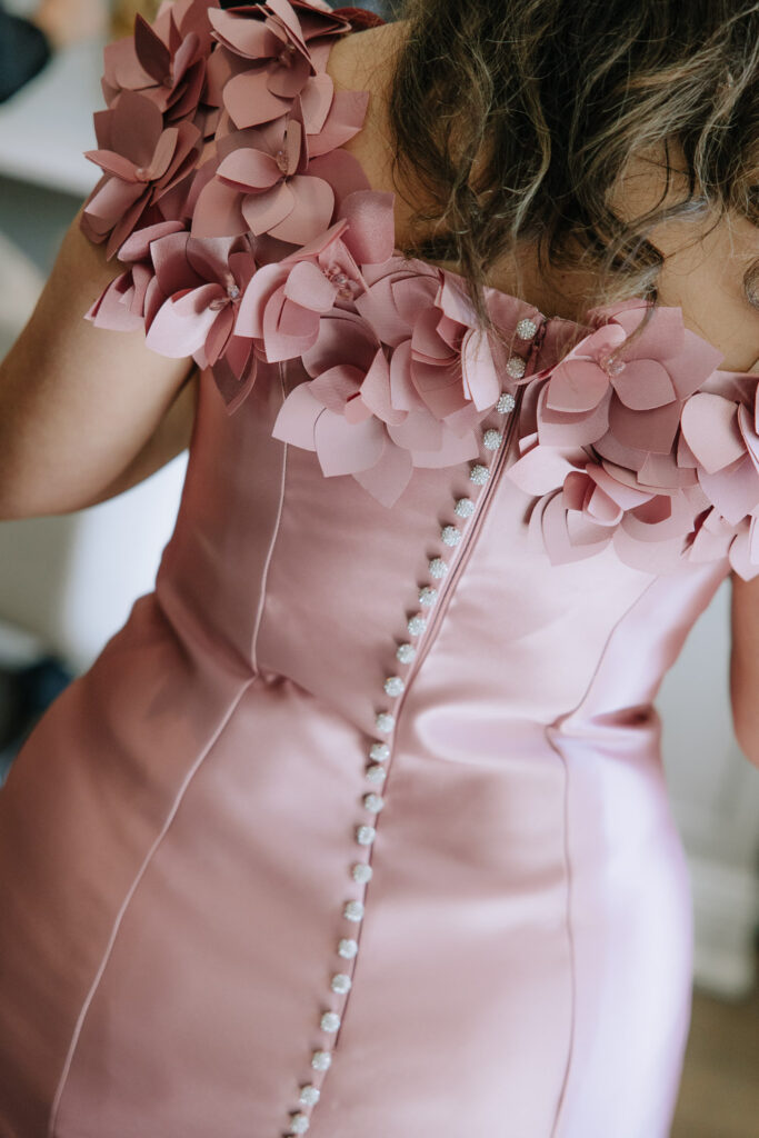 A close-up of the back of a pink dress with flower details and a line of buttons.
