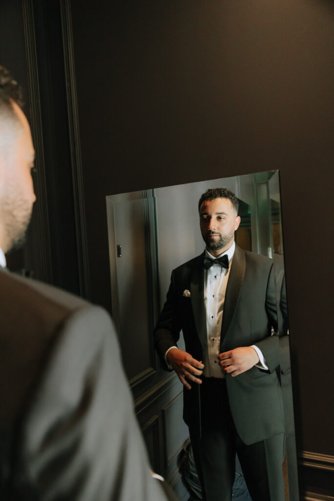 A groom adjusting his tuxedo in a mirror at his Park Chateau Muslim wedding in East Brunswick, New Jersey.