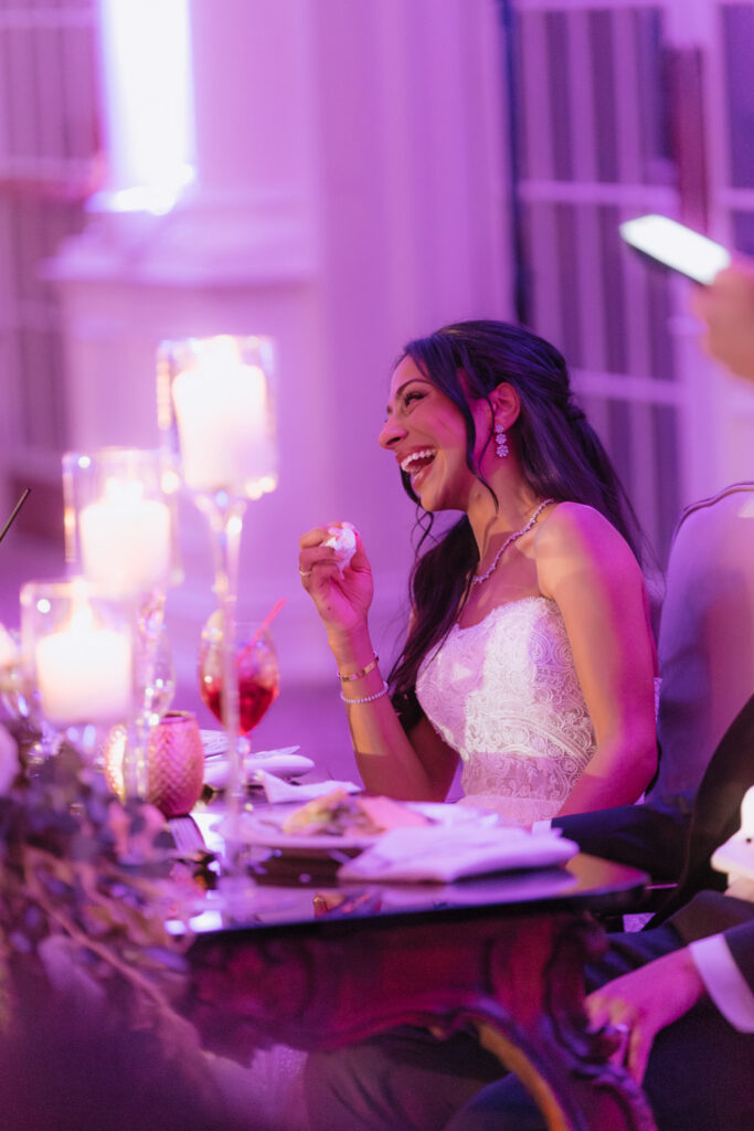 A bride laughs while sitting at a table with candles and drinks at a Park Chateau wedding.