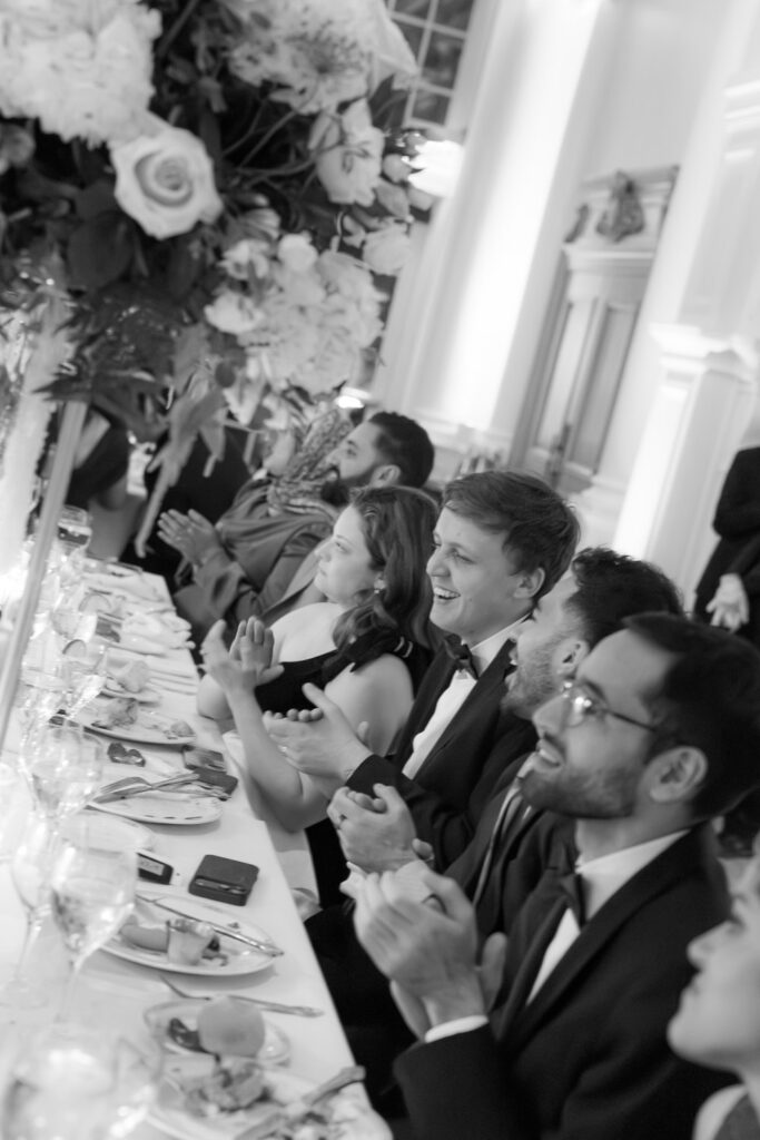 Wedding guests applaud at a table with plates and glasses during a Park Chateau Estate & Gardens wedding.