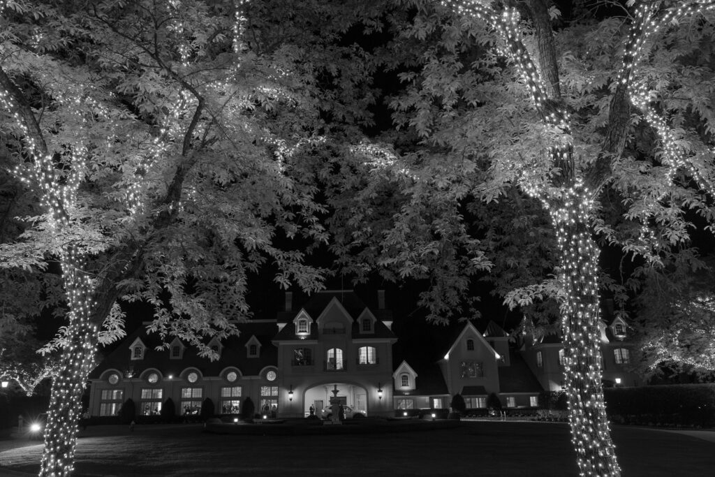 An illuminated Park Château Estate & Gardens building at night framed by trees wrapped in lights.