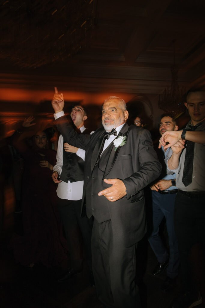 A man in a tuxedo dances with guests at a Park Chateau wedding reception in New Brunswick, New Jersey.