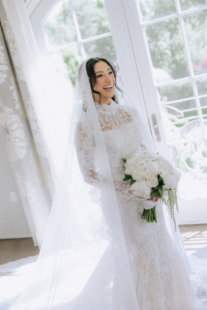 Bride in a long-sleeved lace wedding gown holding a white rose bouquet at Park Chateau.