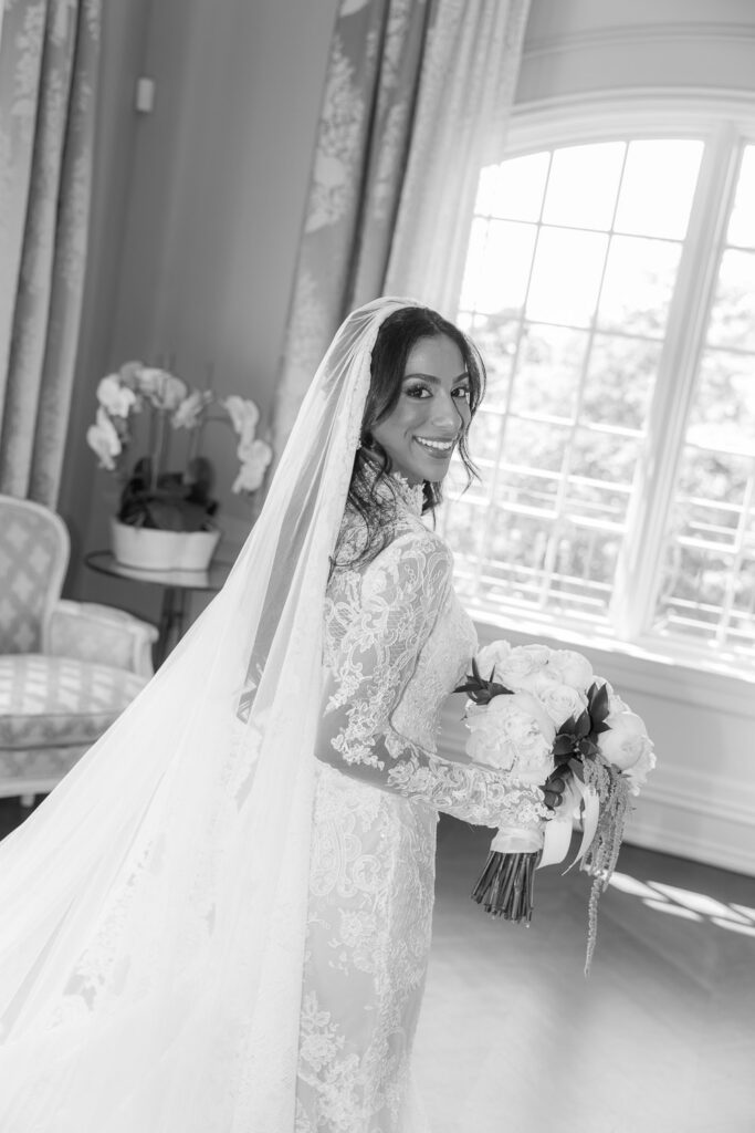 Menah, the bride, in her long-sleeved lace wedding dress, veil, and white bouquet at Park Chateau.