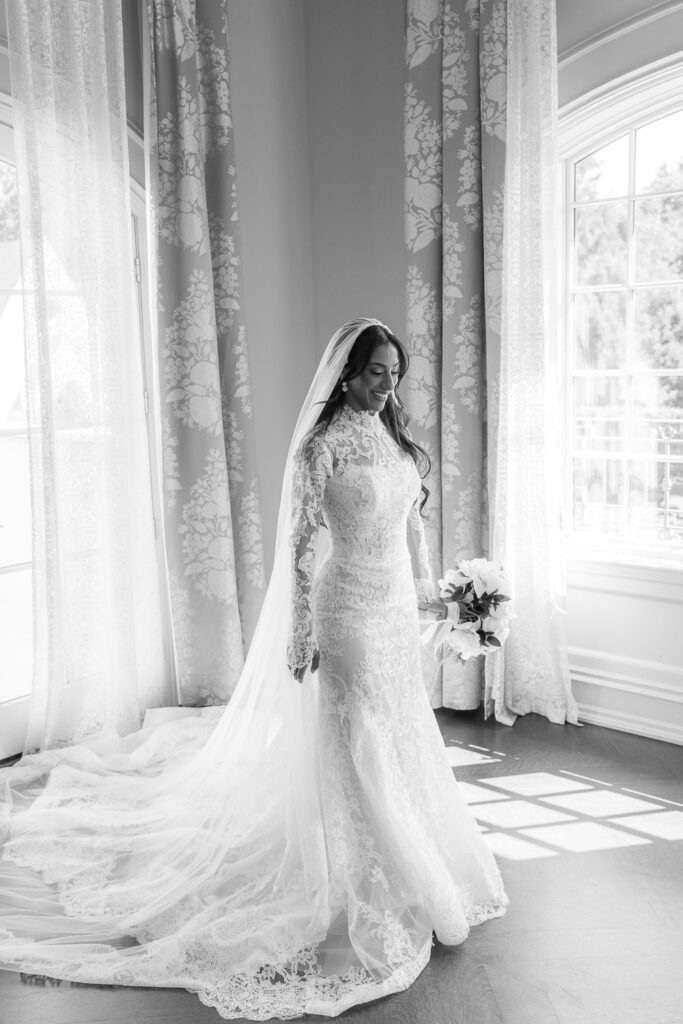 A bride in a long-sleeved lace gown and veil holds a bouquet at Park Chateau New Brunswick New Jersey.