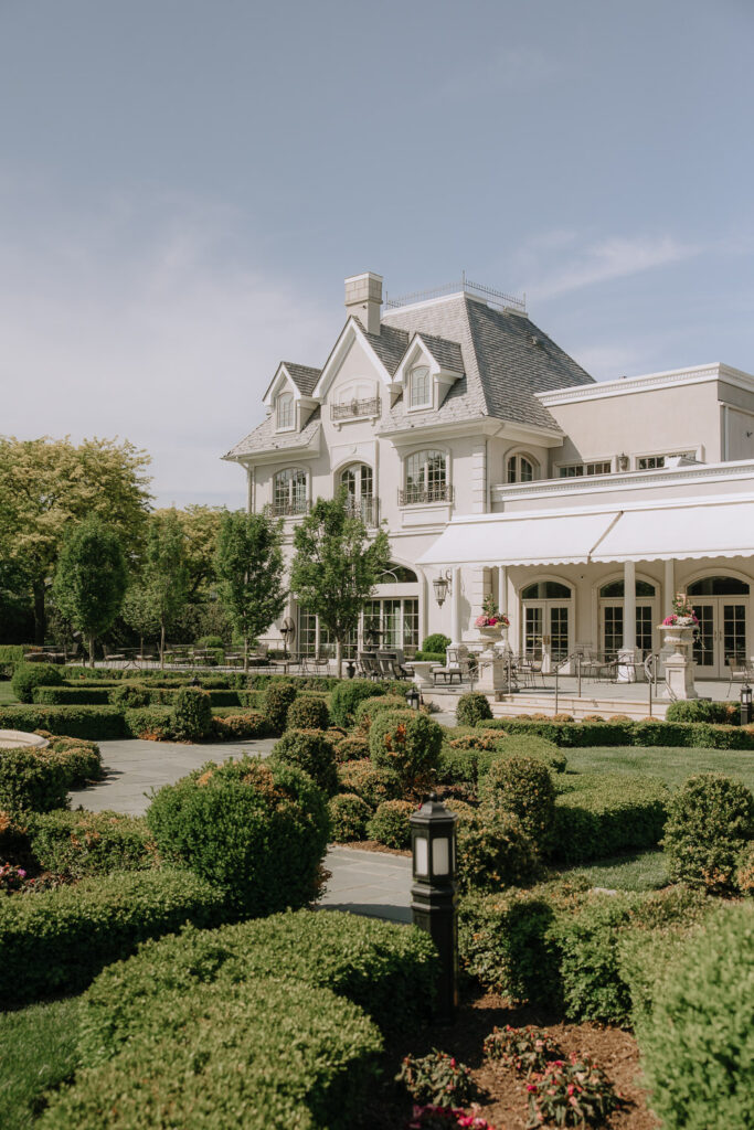 A large, elegant white estate with a gray roof and formal gardens at Park Château, New Jersey.