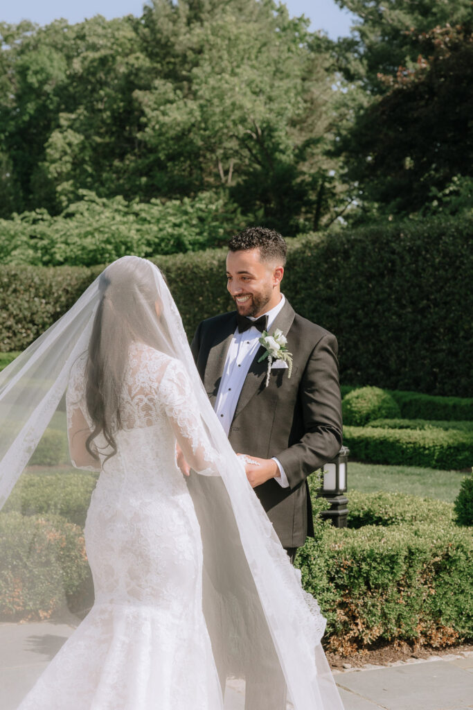 A groom smiles at his bride, whose long veil and hair flow, at Park Chateau Estate & Gardens.
