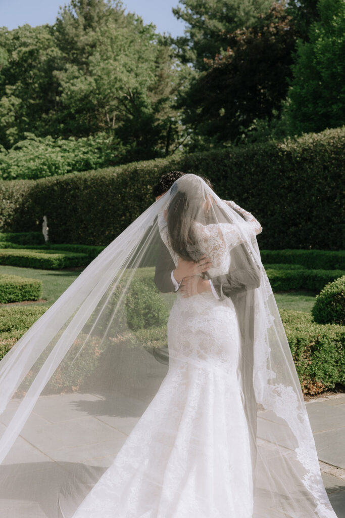 A groom embraces his bride, whose long veil flows around her, at Park Château Estate & Gardens.