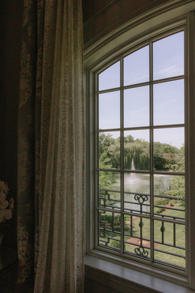 View through a window of a fountain in a lake and lush greenery at Park Chateau in New Jersey.