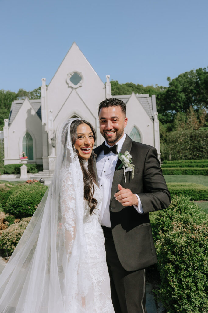 A smiling wedding couple poses outside the Park Chateau Estate & Gardens in East Brunswick, New Jersey.